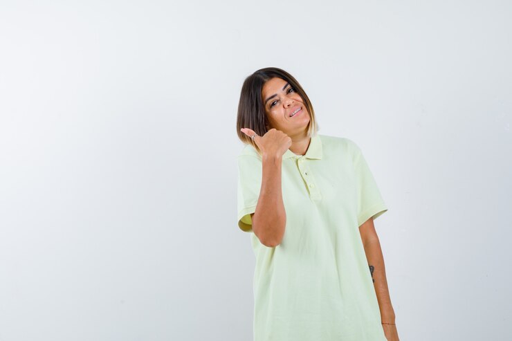 Foto grátis jovem garota em t-shirt apontando para o lado com o polegar e olhando alegre, vista frontal.