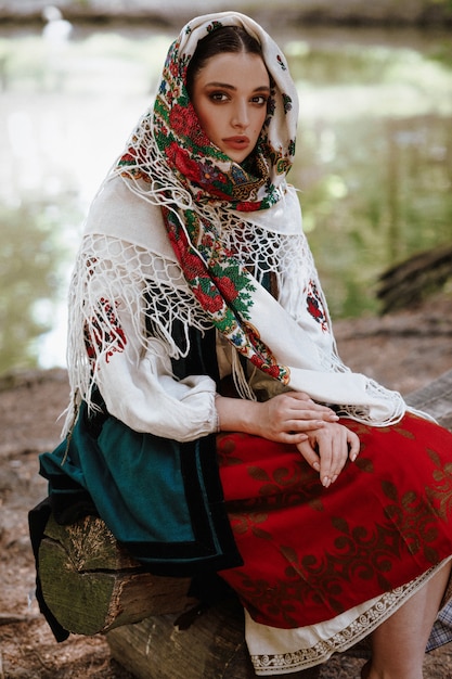 Jovem garota em um vestido bordado tradicional, sentado em um banco perto do lago