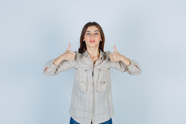 Foto grátis jovem garota em uma camisa bege, jeans mostrando dois polegares para cima e parecendo confiante, vista frontal.