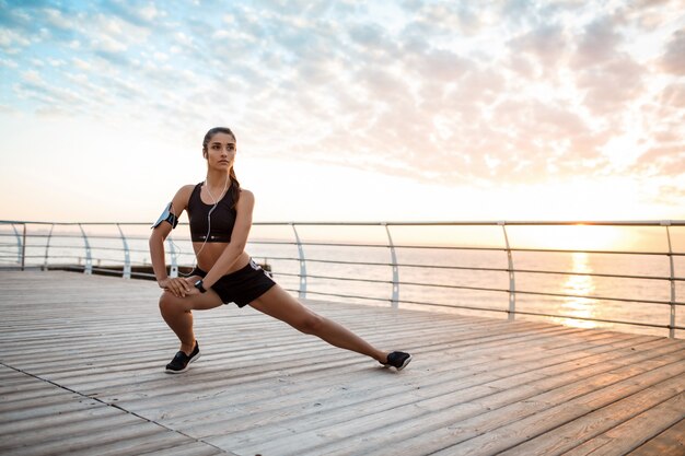 Jovem garota esportiva linda formação ao nascer do sol sobre a beira-mar.