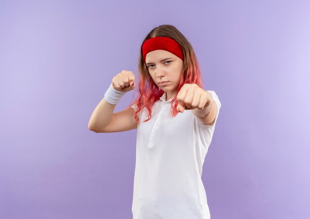 Foto grátis jovem garota esportiva posando como um boxeador com os punhos cerrados em pé sobre a parede roxa