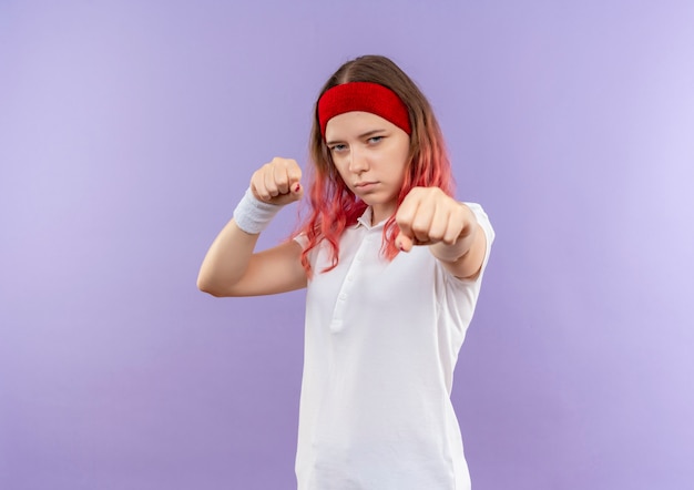 Jovem garota esportiva posando como um boxeador com os punhos cerrados em pé sobre a parede roxa