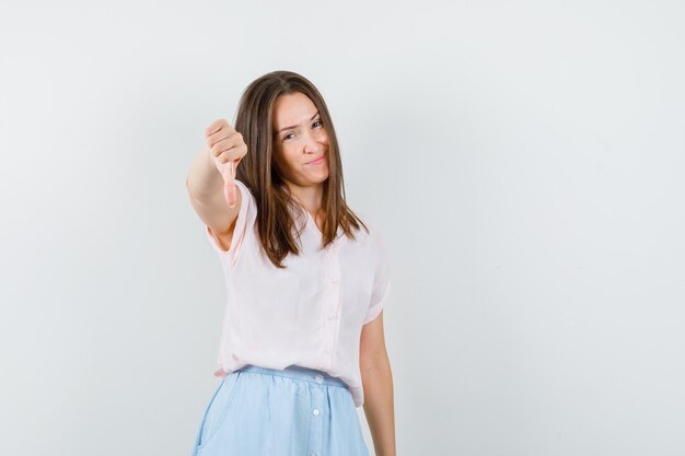 Jovem garota mostrando o polegar para baixo educadamente em t-shirt, vista frontal da saia.