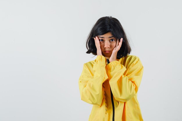 Jovem garota segurando as mãos na cabeça em uma jaqueta amarela e olhando pensativa.