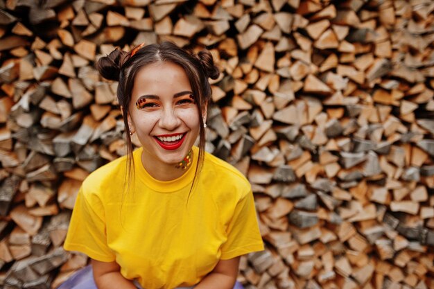 Jovem garota sorridente com maquiagem brilhante vestindo camisa amarela contra fundo de madeira