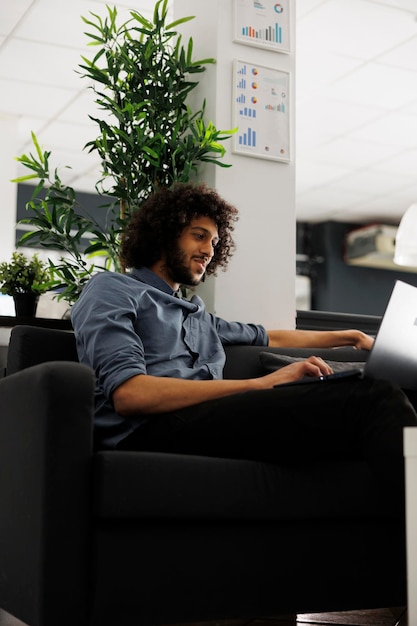 Foto grátis jovem gerente de projeto árabe sorridente trabalhando em um laptop em um escritório de negócios. profissional de marketing feliz analisando uma campanha de promoção de produto bem sucedida em um espaço de coworking