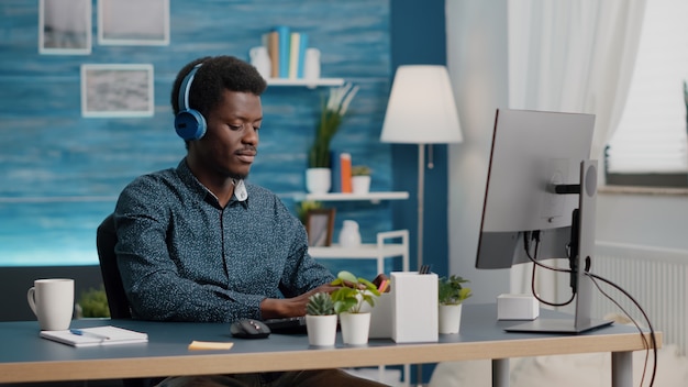 Jovem gerente usando fones de ouvido para ouvir música enquanto trabalha em casa no computador PC