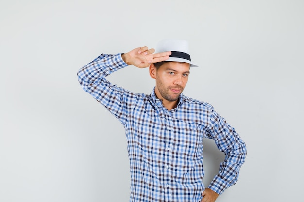 Jovem gesticulando com a mão e os dedos na cabeça em uma camisa xadrez e parecendo confiante.