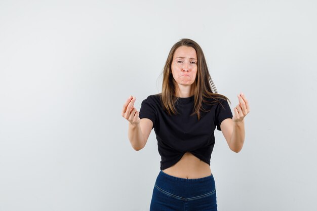 Jovem gesticulando com os dedos na blusa preta, calça e parecendo triste.