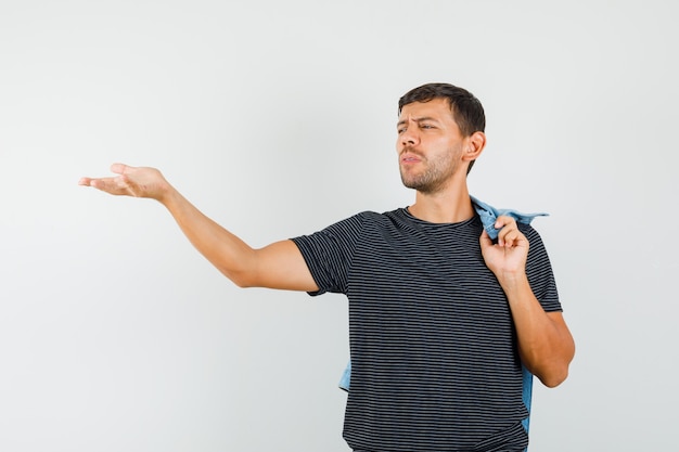 Jovem gesticulando de maneira questionadora, segurando uma jaqueta nas costas da camiseta