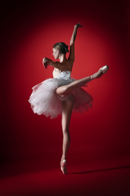 Jovem graciosa bailarina feminina ou bailarina clássica dançando no estúdio vermelho.