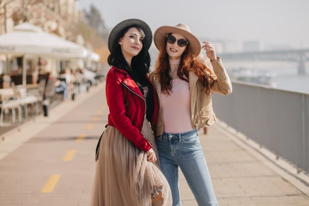 Jovem graciosa com saia bege relaxando com a melhor amiga