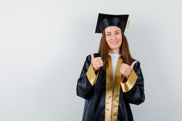 Jovem graduada feminina aparecendo em um vestido acadêmico e parecendo feliz, vista frontal.