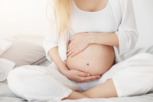 Jovem grávida em breve ser mãe tocando sua barriga sentada em seu quarto à tarde. Conceito de gravidez.