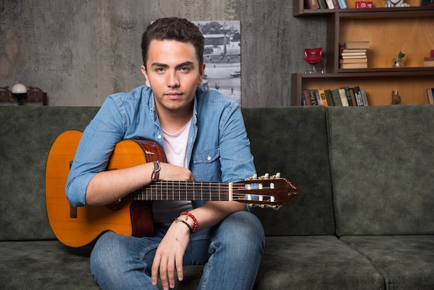 Jovem guitarrista segurando uma bela guitarra e sentado no sofá. foto de alta qualidade