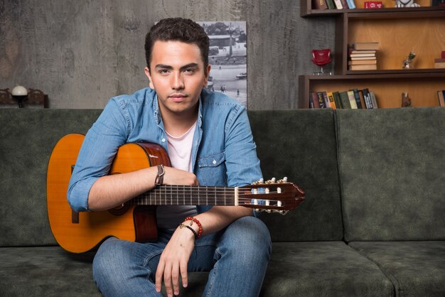 Jovem guitarrista segurando uma bela guitarra e sentado no sofá. Foto de alta qualidade