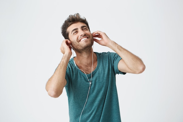 Jovem hipster sorridente bronzeado pelo sol, desfrutando de boas faixas usando o aplicativo de música grátis no gadget. tiro de boa aparência cheia de alegria homem barbudo