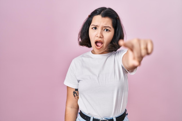 Foto grátis jovem hispânica vestindo camiseta branca casual sobre fundo rosa apontando descontente e frustrado para a câmera, zangado e furioso com você