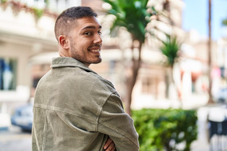 Foto grátis jovem hispânico sorrindo confiante em pé com gesto de braços cruzados na rua