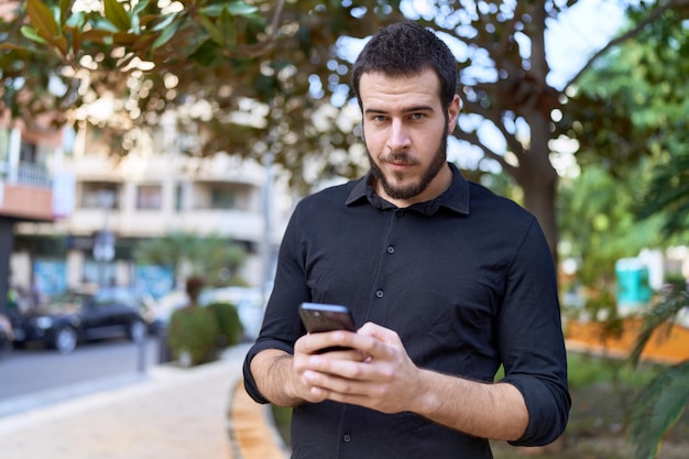 Jovem hispânico sorrindo confiante usando smartphone no parque