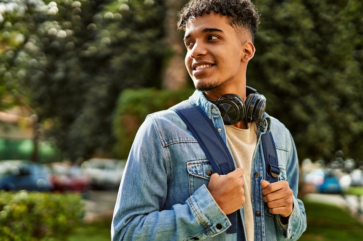 Foto grátis jovem hispânico sorrindo usando fones de ouvido no campus da universidade