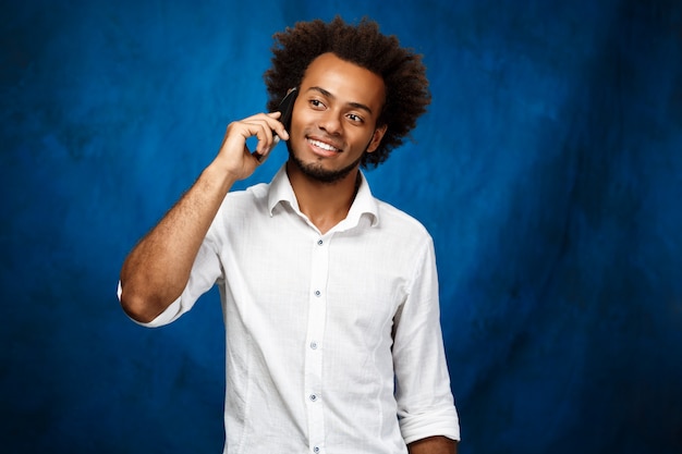 Jovem homem Africano bonito falando no telefone sobre parede azul.