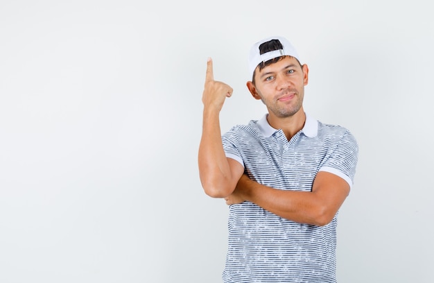 Jovem homem apontando para cima com camiseta e boné e parecendo alegre