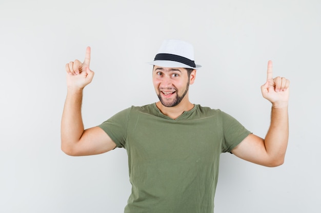 Jovem homem apontando para cima com uma camiseta e um chapéu verdes e parecendo alegre