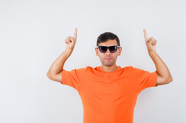 Jovem homem apontando para cima com uma camiseta laranja e parecendo confiante