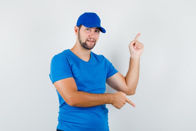 Jovem homem apontando para cima e para baixo com camiseta azul e boné e olhar positivo