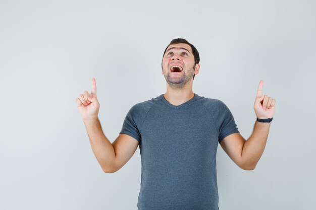 Jovem homem apontando para cima em uma camiseta cinza e parecendo feliz