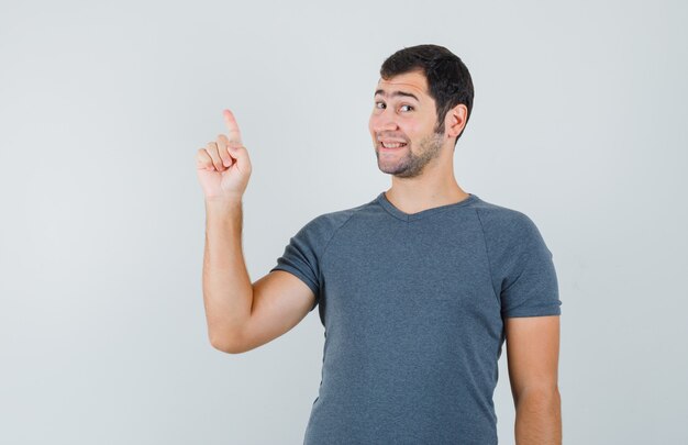 Jovem homem apontando para cima em uma camiseta cinza e parecendo feliz