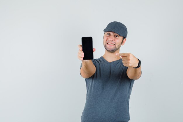 Jovem homem apontando para o celular com boné da camiseta e parecendo feliz