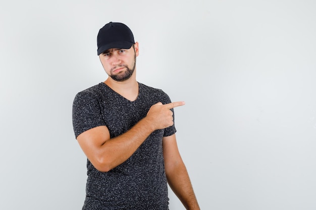 Jovem homem apontando para o lado com camiseta e boné e parecendo desapontado