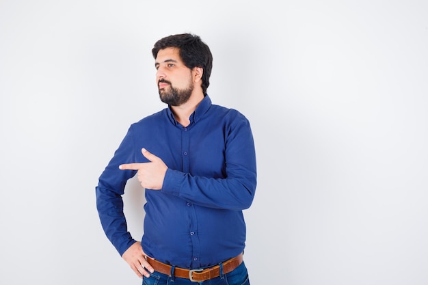 Jovem homem apontando para o lado esquerdo em uma camisa, jeans e parecendo focado. vista frontal.