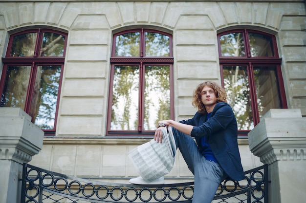 Foto grátis jovem homem avermelhado lendo jornal perto de edifício de estilo antigo