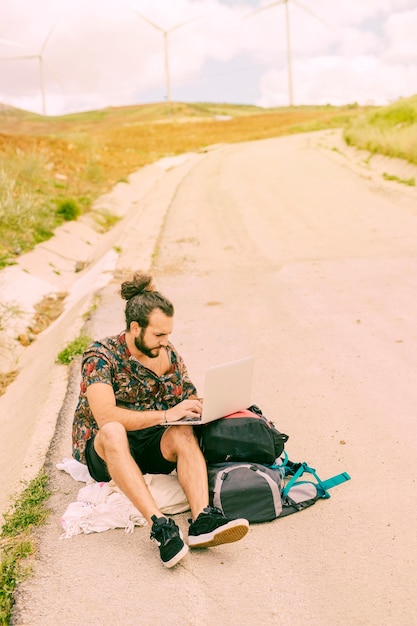 Jovem homem barbudo usando laptop sentado na estrada