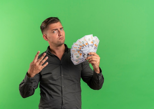 Foto grátis jovem homem bonito loiro irritado com dinheiro e quatro gestos isolados em um fundo verde com espaço de cópia