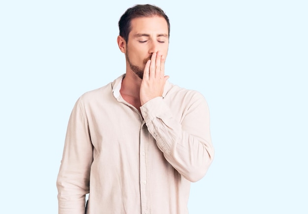 Foto grátis jovem homem caucasiano bonito vestindo roupas casuais entediado bocejando cansado cobrindo a boca com a mão. inquietação e sonolência.
