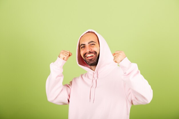 Jovem homem caucasiano com capuz rosa isolado, punho cerrado feliz com sucesso no gesto de vencedor