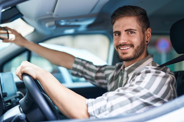 Jovem homem caucasiano tocando o retrovisor sentado no carro na rua