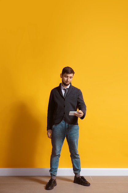 Jovem homem caucasiano usando retrato de corpo inteiro em smartphone isolado na parede amarela