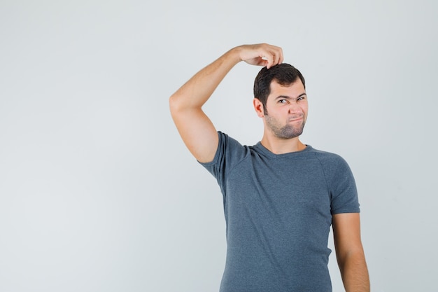 Jovem homem coçando a cabeça em uma camiseta cinza e parecendo hesitante