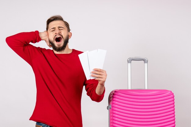 Jovem homem com bolsa rosa segurando os bilhetes na parede branca, voo colorido, viagem turística, foto, emoção