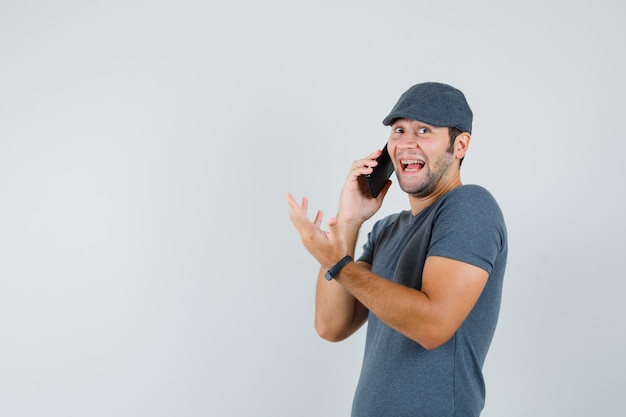 Jovem homem com boné de camiseta falando no celular e parecendo feliz