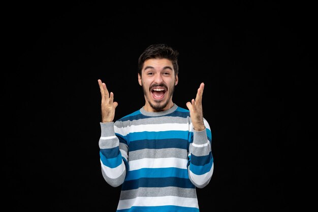 Jovem homem com camisa listrada azul, de frente, emocionando-se na parede preta