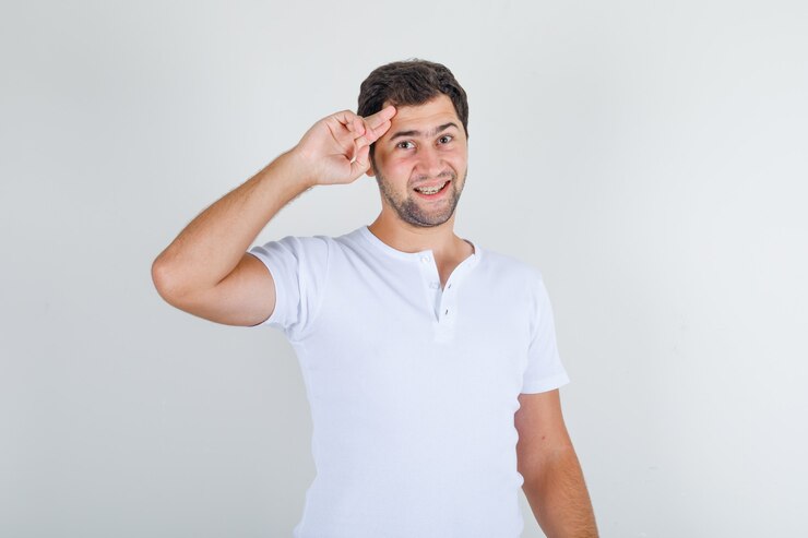 Foto grátis jovem homem com camiseta branca com dois dedos nas têmporas e parecendo alegre