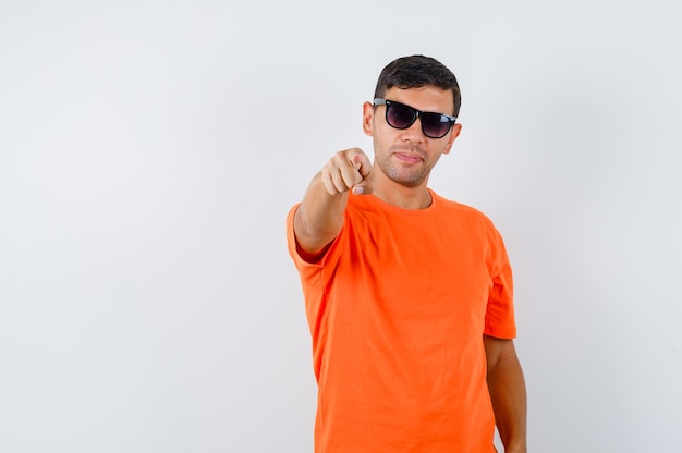 Jovem homem com camiseta laranja apontando para a câmera e parecendo confiante