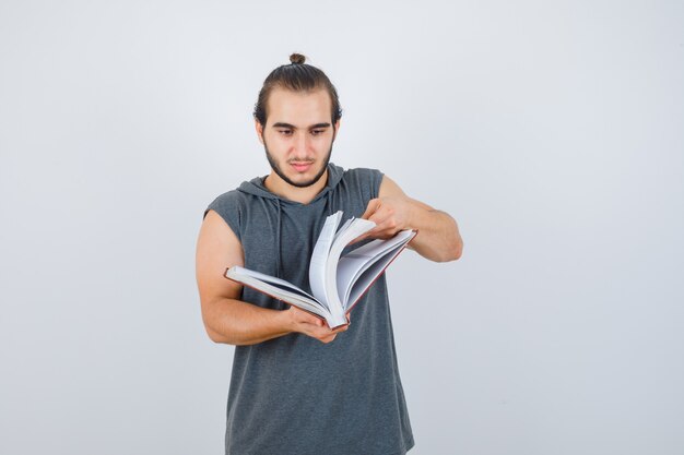 Jovem homem com capuz sem mangas olhar através do livro e parecendo confiante, vista frontal.