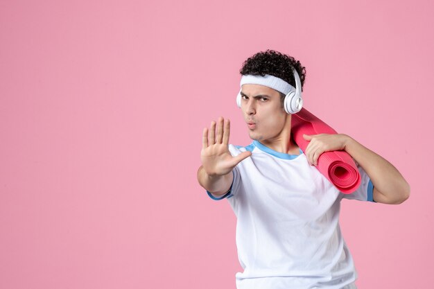 Jovem homem com roupas esportivas e tapete de ioga na parede rosa